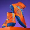 A pair of high-top orange athletic shoes with blue soles is showcased on an orange pedestal, set against a purple background, fusing functionality and style.