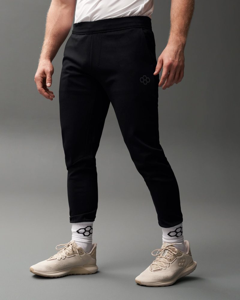 This image showcases a man wearing black athletic pants and light-colored sneakers presenting a sporty and stylish look ideal for workouts or casual wear