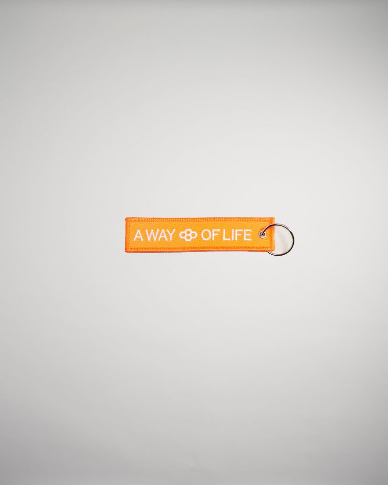 An orange fabric tag with the text A WAY OF LIFE displayed prominently attached to a metal keyring