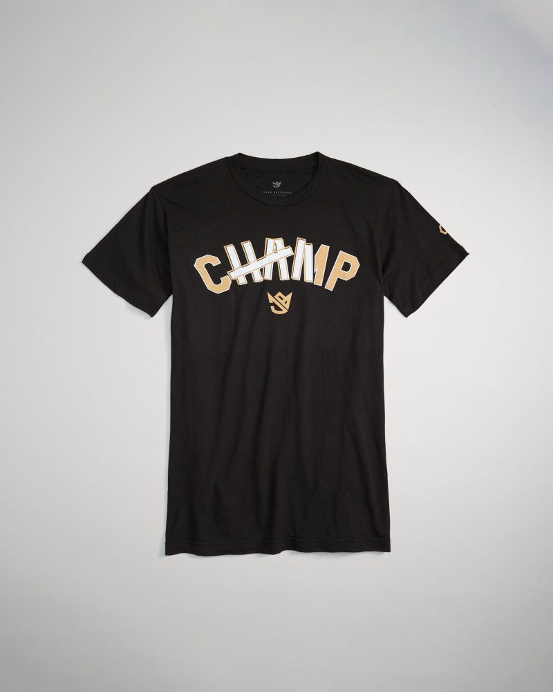 A black t-shirt featuring a partially crossed-out CHAMP text in bold golden letters highlighting a playful twist on the classic champion motif