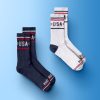 Two pairs of socks in navy blue and white, showcasing 'USA' branding and stylish stripes, are featured against a light blue gradient background.