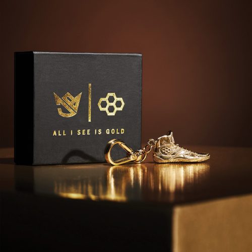 A luxurious gold sneaker keychain sits beside an elegant black box featuring the phrase ALL I SEE IS GOLD