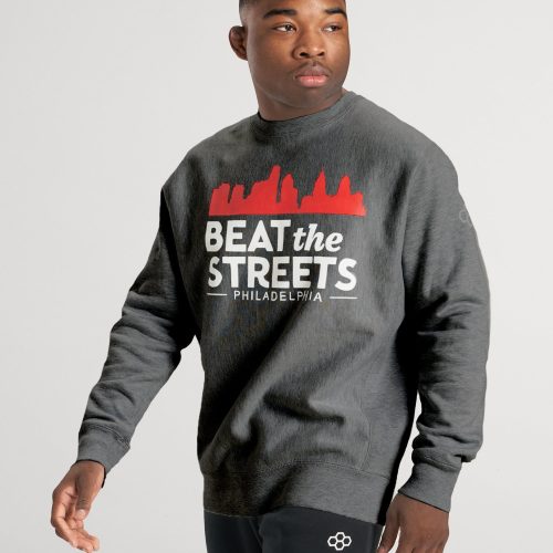 A young man wearing a gray sweatshirt with the phrase BEAT the STREETS PHILADELPHIA and black pants featuring a white logo posing confidently against a soft gray background